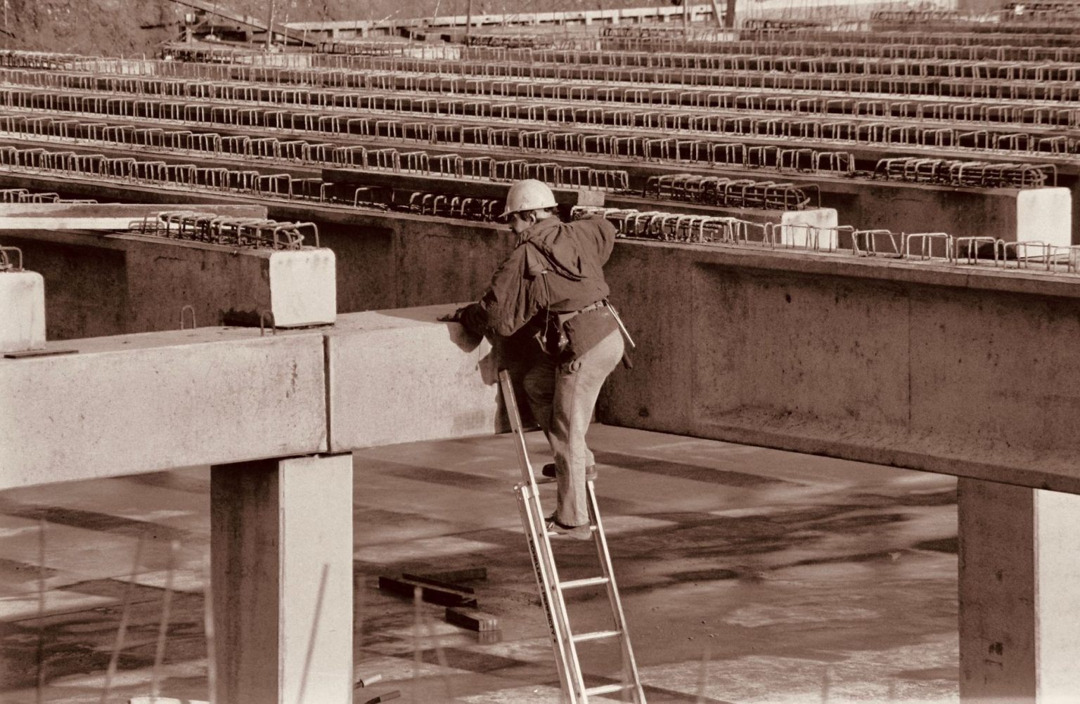 Trabalhador usando equipamentos de segurança sobe uma escada vertical em uma estrutura industrial.