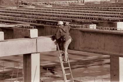 Trabalhador usando equipamentos de segurança sobe uma escada vertical em uma estrutura industrial.