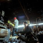 Trabalhadores realizam atividades junto a máquinas em uma fábrica.