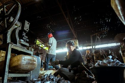 Trabalhadores realizam atividades junto a máquinas em uma fábrica.