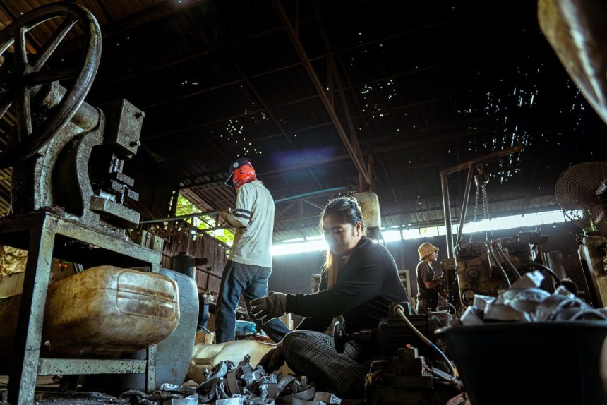 Trabalhadores realizam atividades junto a máquinas em uma fábrica.