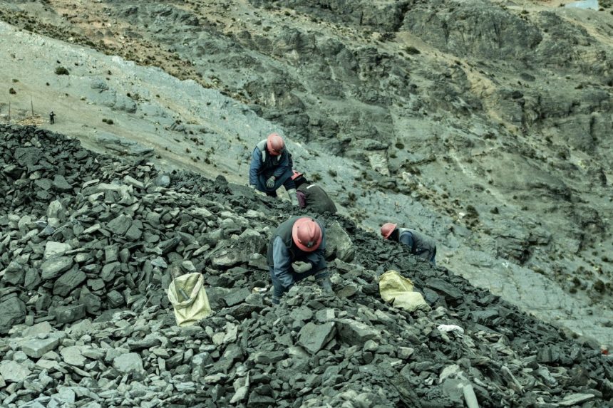 Trabalhadores usando capacetes recolhem pedras em uma pedreira vista de cima.