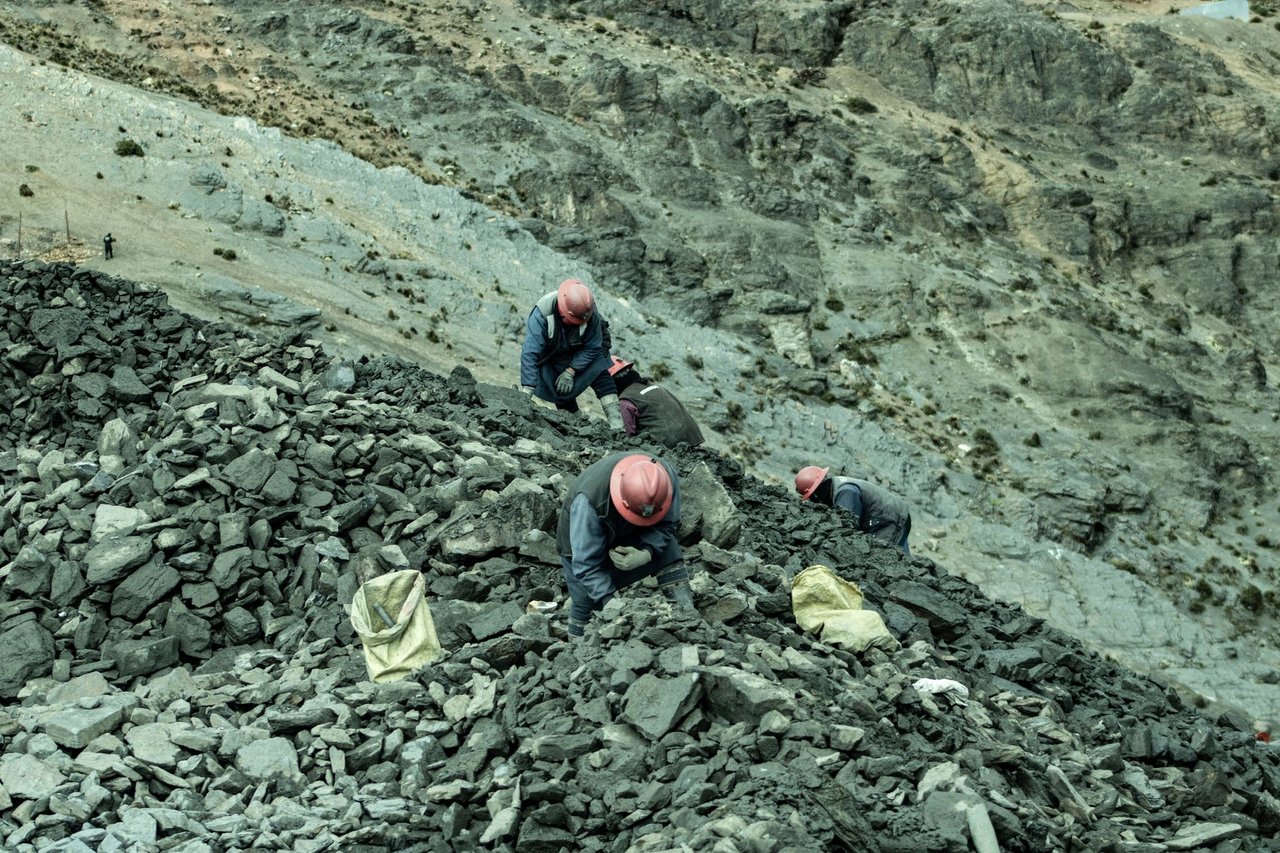 Trabalhadores usando capacetes recolhem pedras em uma pedreira vista de cima.