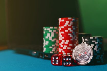 Fichas e dados de cassino sobre uma mesa ao lado de um laptop, representando apostas online.